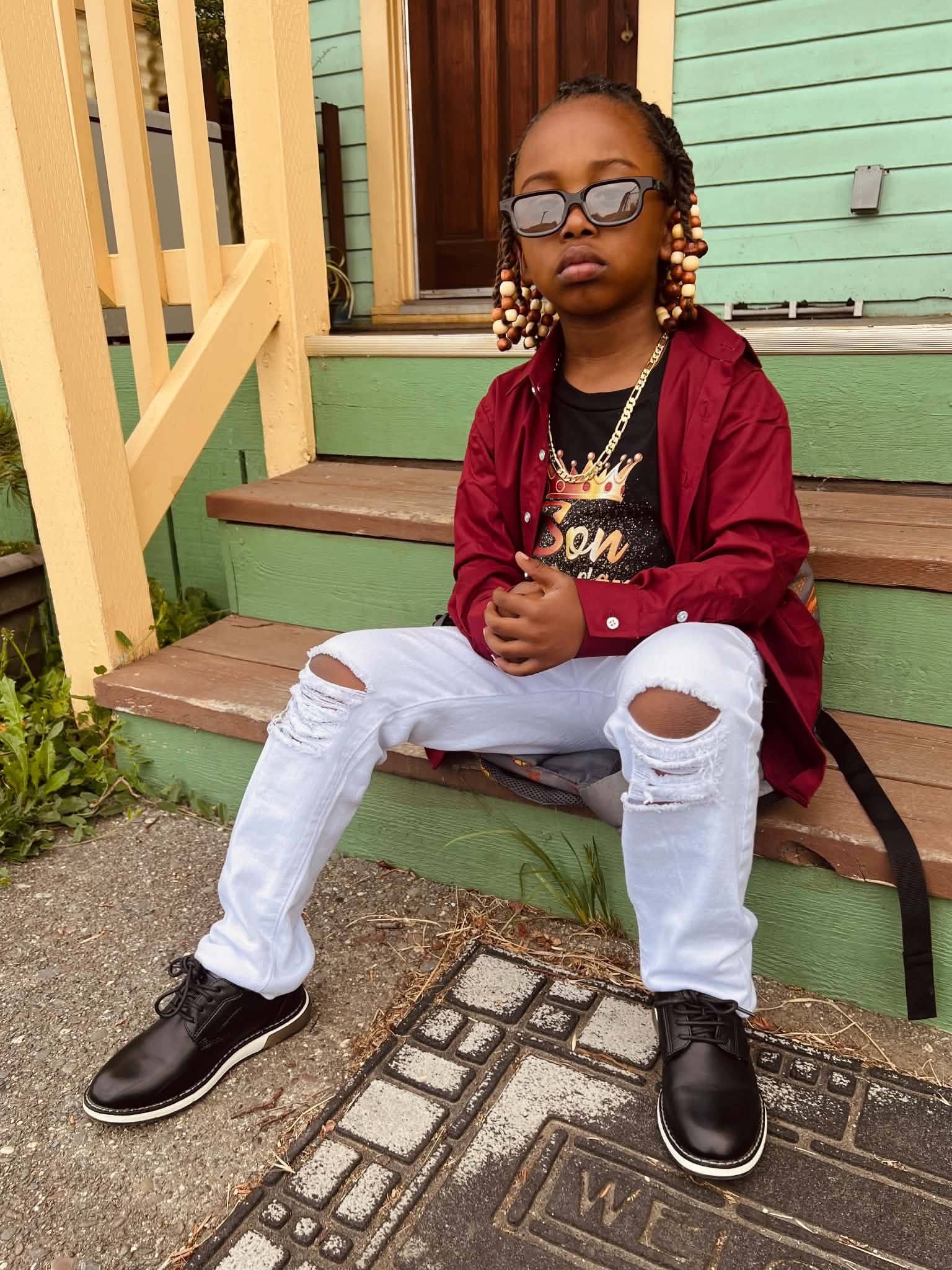Child seated on porch steps in a burgundy jacket
