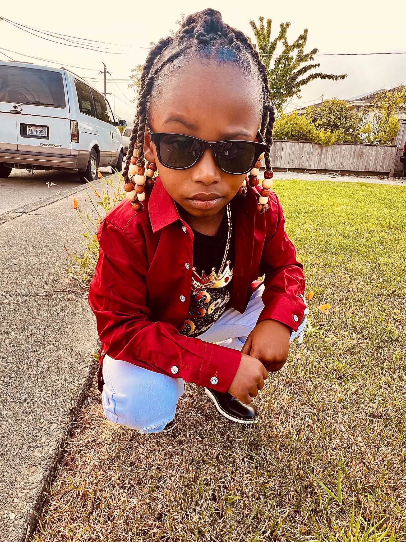 Child posing outdoors in a red jacket and sunglasses