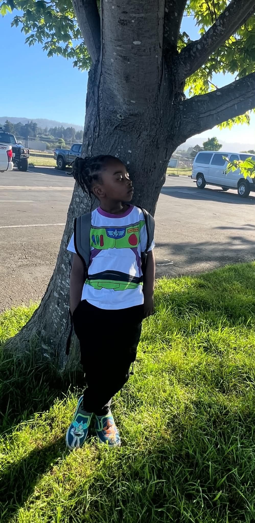Child standing beside a tree with a backpack