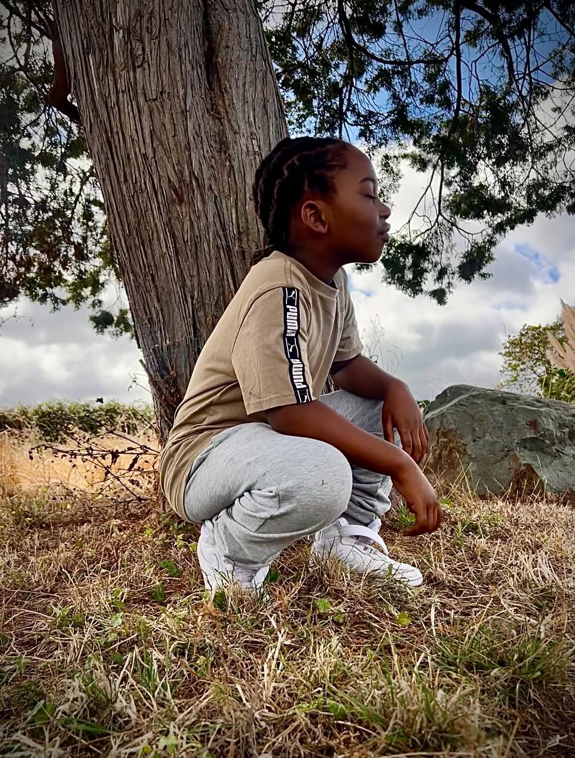 Child resting beside a large tree during an outdoor adventure