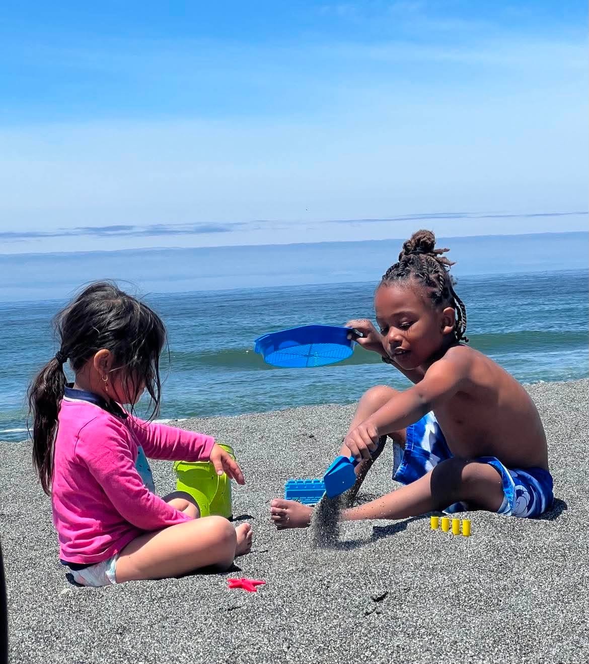 Children playing with sand toys by the ocean