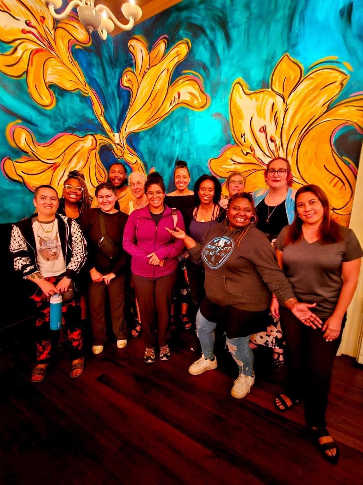 Community group standing together before a colorful floral mural