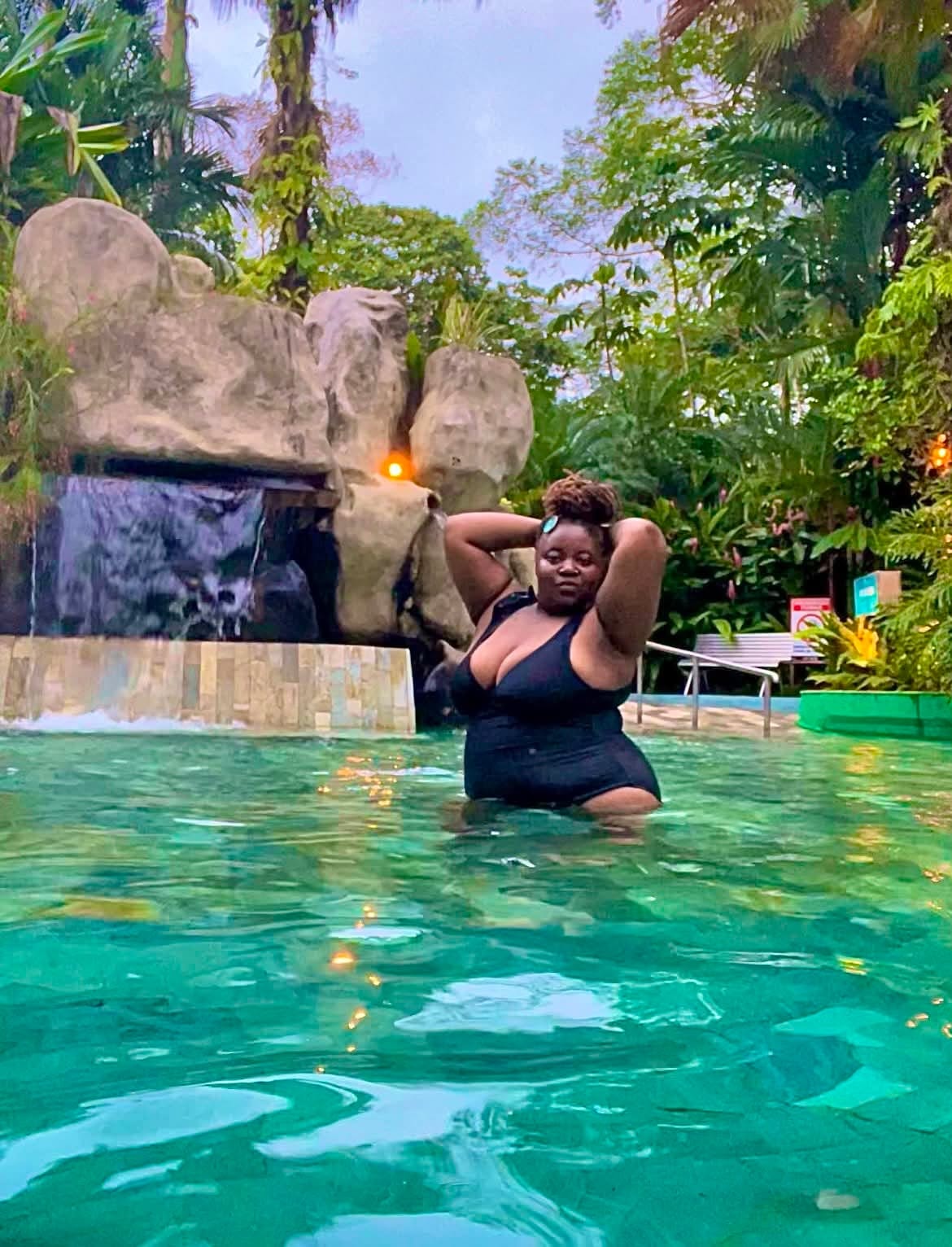 Community member enjoying a tropical pool beside a waterfall
