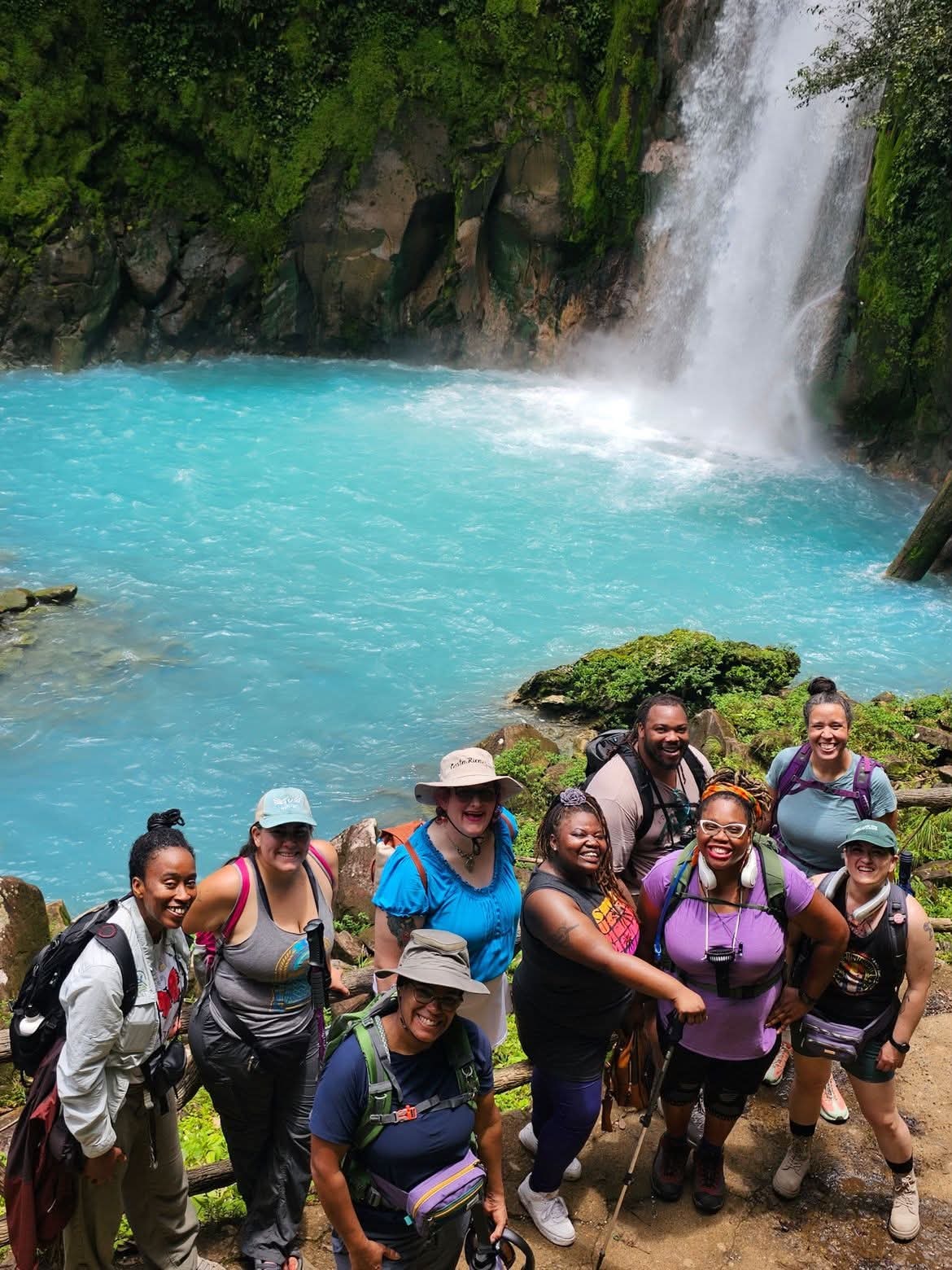 Travel group gathered beside a turquoise waterfall